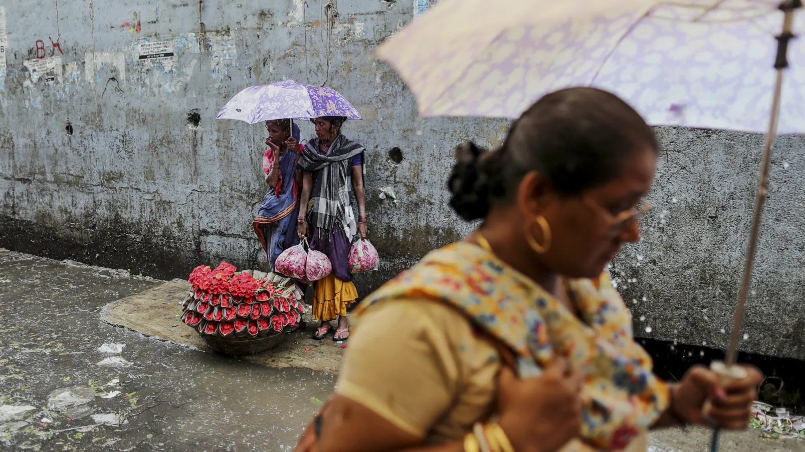 Flower vendors take shelter from the rain under an umbrella at the Dadar wholesale flower market in Mumbai.
