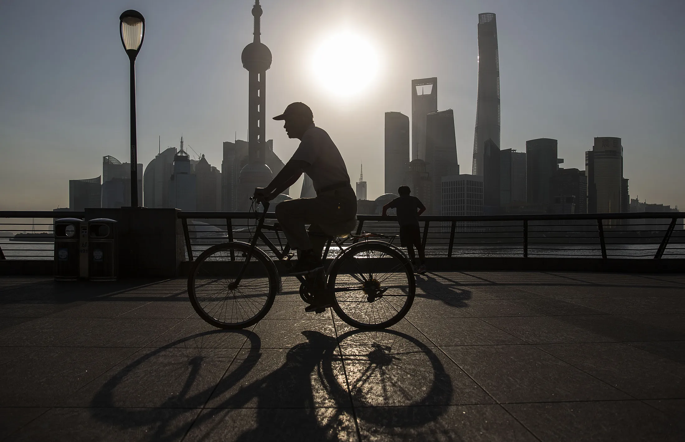 A man rides a bicycle along the Bund while buildings of Pudong's Lujiazui financial district stand across the Huangpu River as the sun rises in Shanghai, China, on Friday, Oct. 2, 2015.