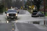A truck drives through water over a road near Everson, Wash., Monday, Nov. 29, 2021 past a car that was stranded by flooding in the area earlier in the month. Localized flooding was expected Monday in Washington state from another in a series of rainstorms, but conditions do not appear to be as severe as when extreme weather hit the region earlier in November. (AP Photo/Elaine Thompson)