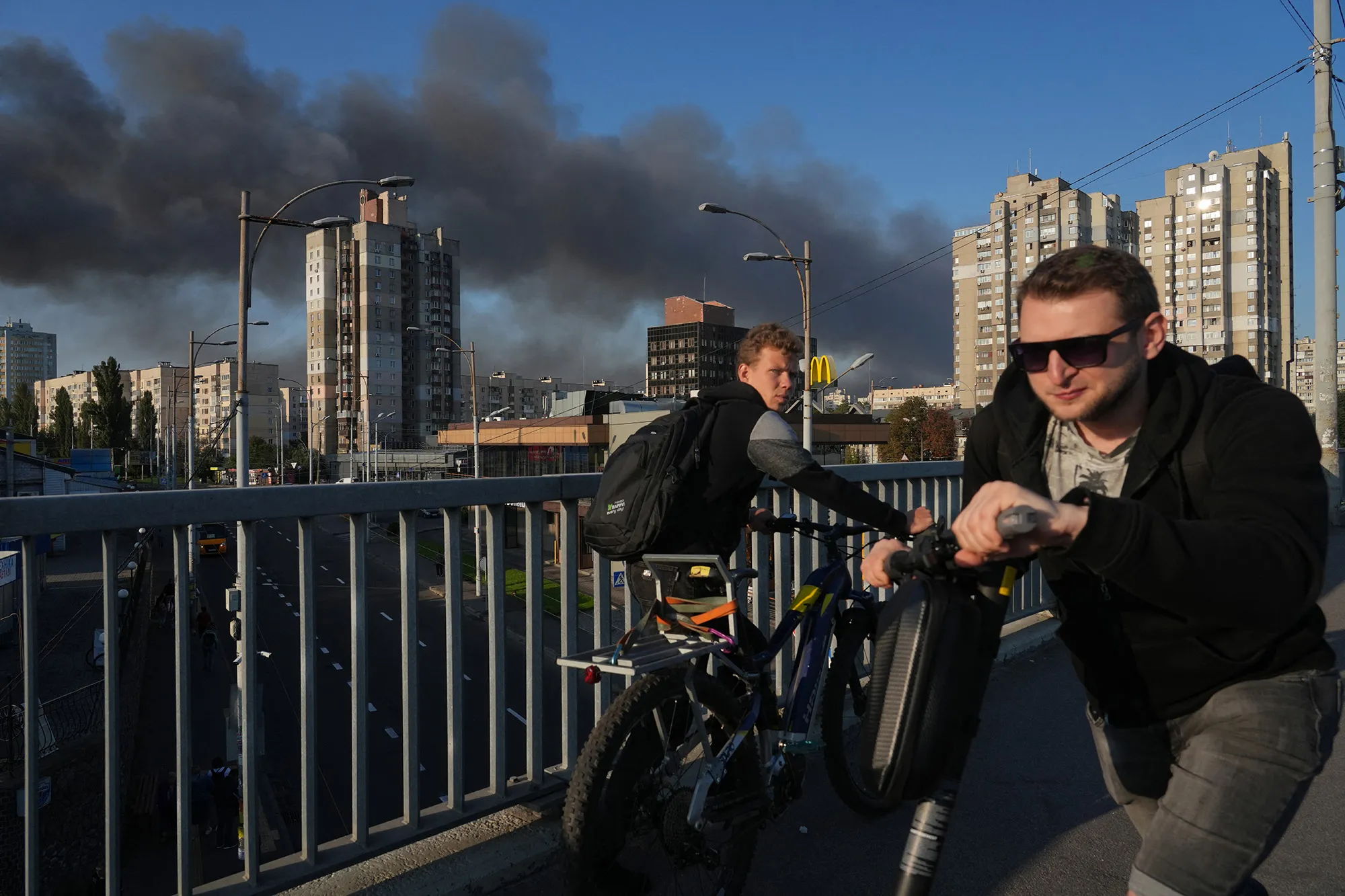 Local residents walk across a bridge as smoke rises following Russian drone and missile strike in Kyiv on Sept. 7.&nbsp;