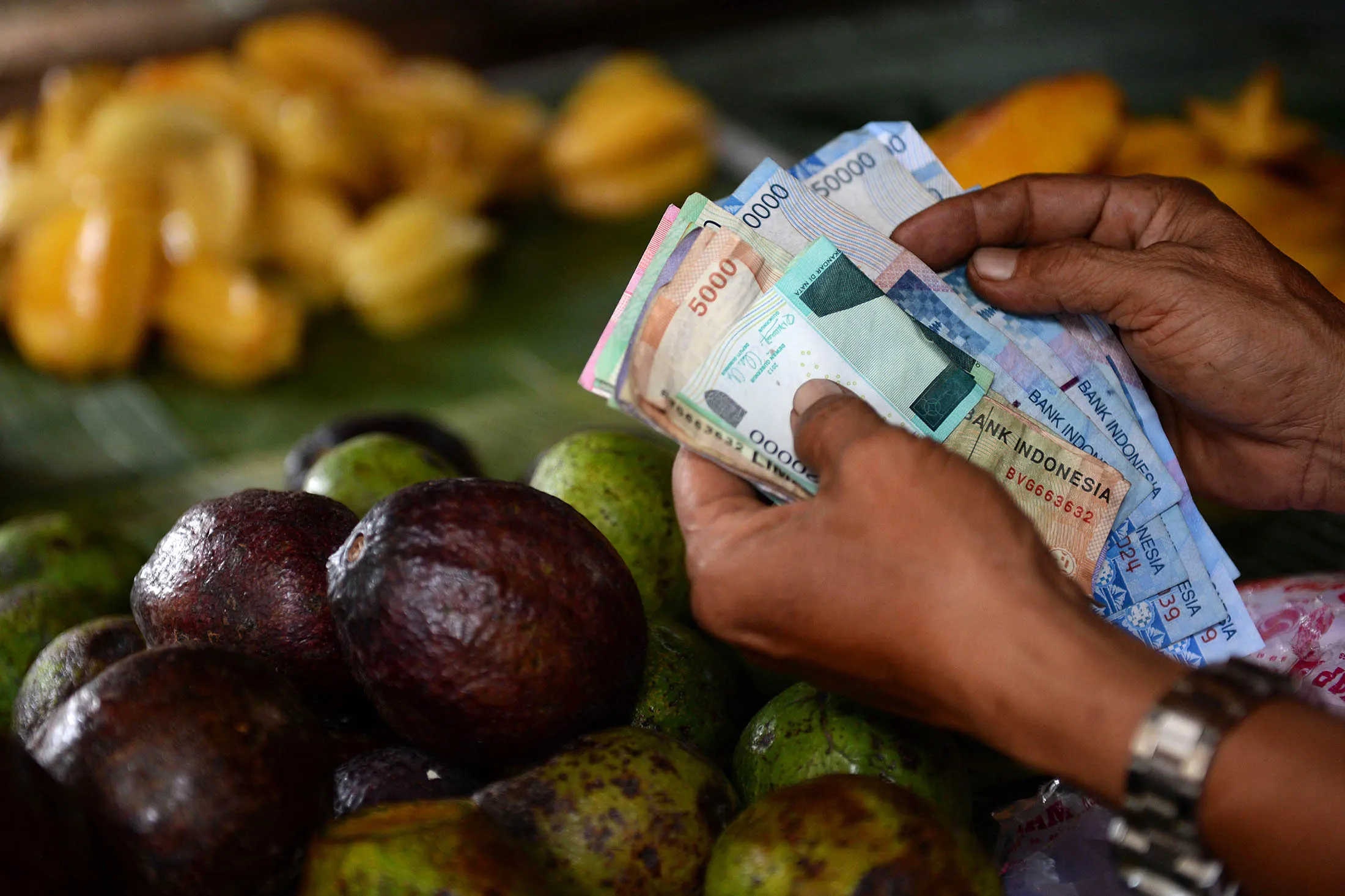 A fruit vendor counts various Indonesian rupiah banknotes at his market stall in Jakarta, Indonesia, on Wednesday, June 18, 2014. The parliament budget commission approved a revised 2014 budget deficit of 2.4 percent of gross domestic product, Chairman Ahmadi Noor Supit said in Jakarta on June 18.
