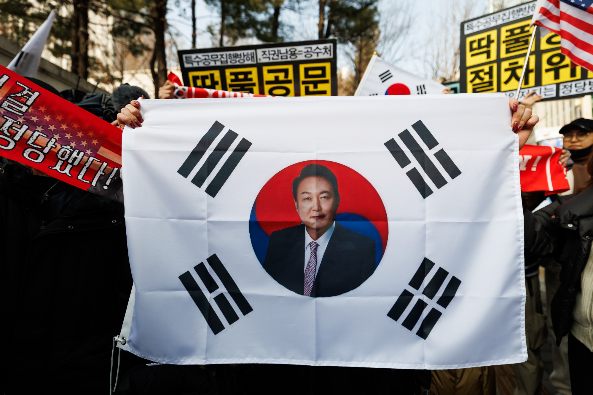 A supporter of former South Korean President Yoon Suk Yeol holds a flag outside the Seoul Central District Court in Seoul, South Korea, on Friday, Jan. 16, 2026. Yoon was sentenced to five years in jail for charges including resisting arrest, marking the disgraced ex-leader's first sentence in a slew of pending cases connected to his declaration of martial law. Photographer: SeongJoon Cho/Bloomberg