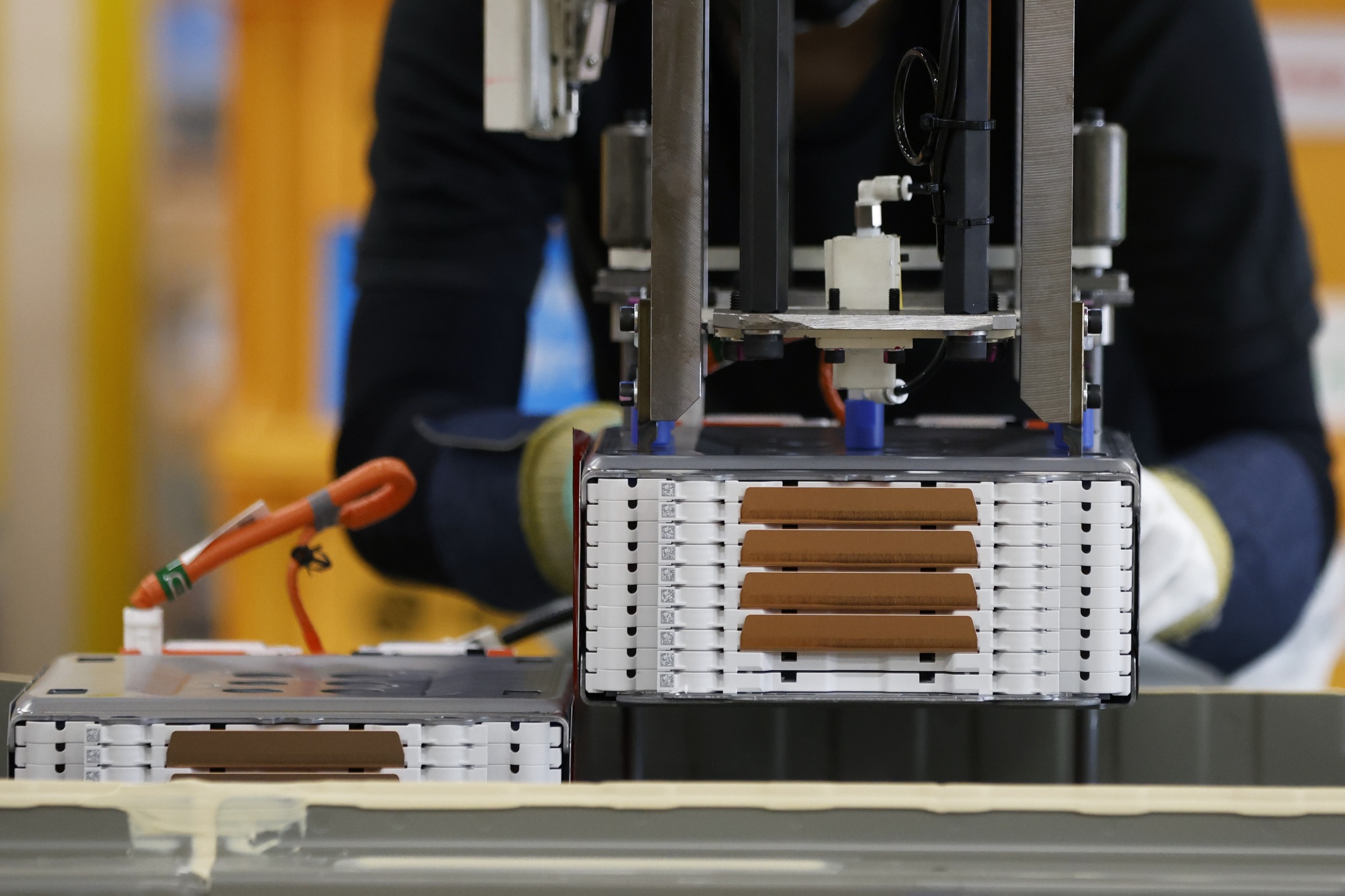 A worker installs a stack of lithium-ion batteries onto a battery pack for an electric vehicle in Japan.