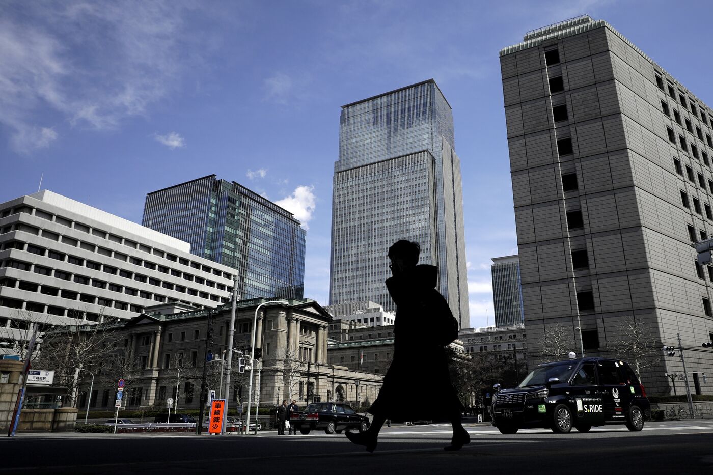 A pedestrian is silhouetted while walking past the Bank of Japan (BOJ) headquarters, left, in Tokyo.