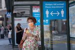 A woman wears a face mask as she waits at a bus stop with an information sign asking people to keep social distance on June 26, 2020 in Stockholm, Sweden.