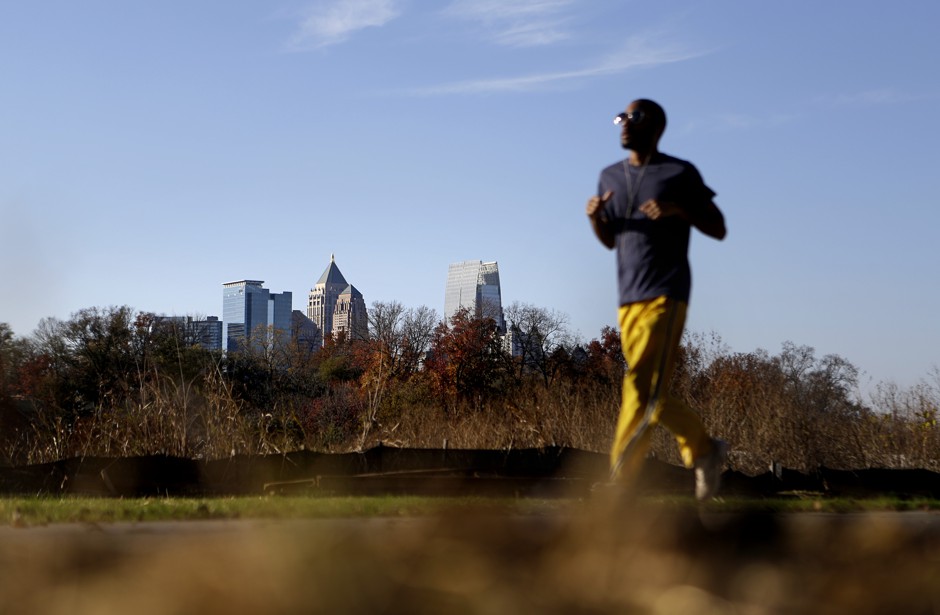 A man jogs along the Atlanta BeltLine park as Midtown high-rises stand in the background. Long greenway parks like the BeltLine are linked with gentrification in cities.