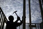 A contractor is seen hammering a nail into wood framing for a house under construction 