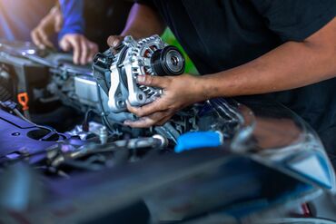 Mechanic is repairing and replacing a battery charger at car service center. Mechanic man holding alternator of the car in repair and maintenance garage.