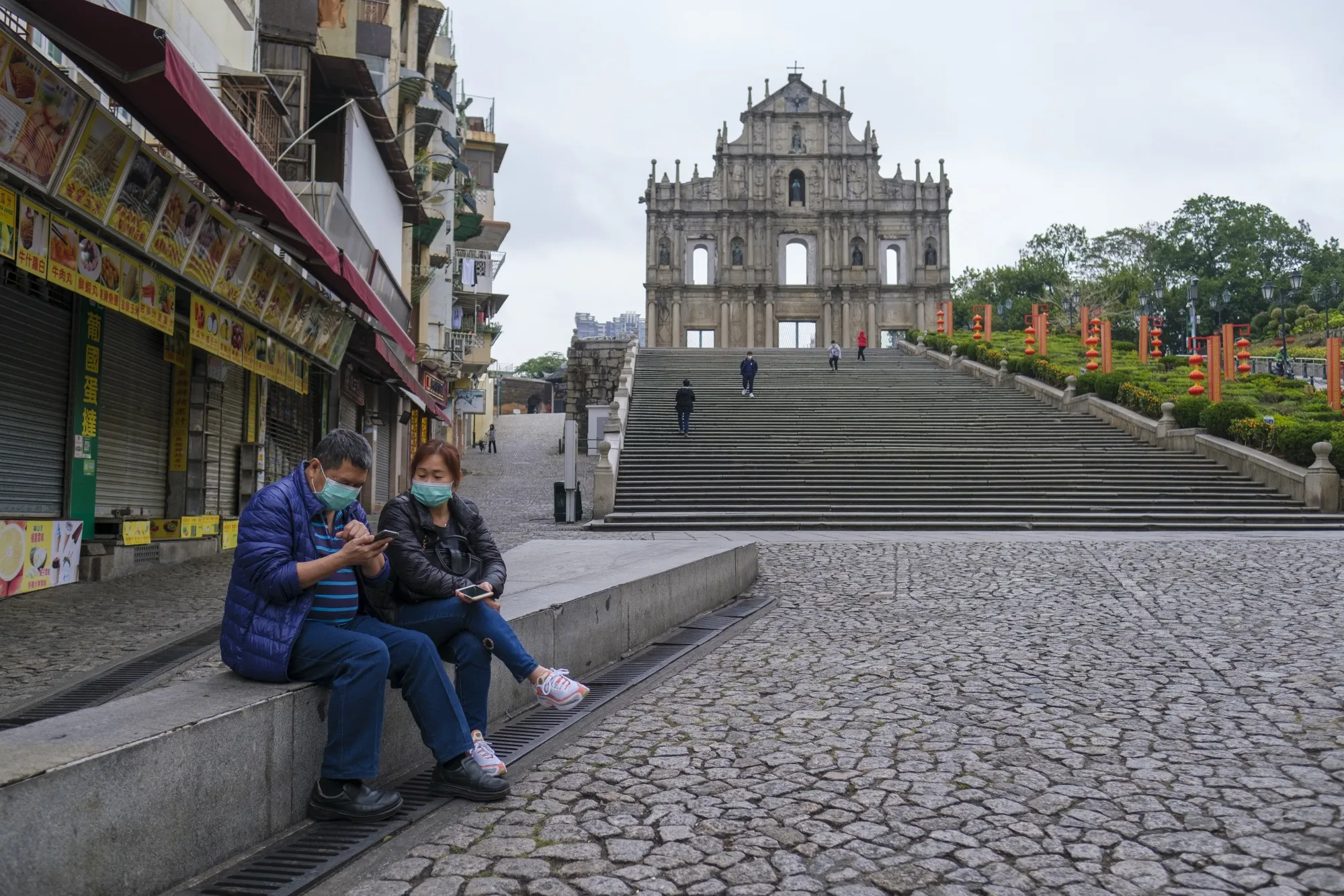 Pedestrians wearing protective face masks sit near the Ruins of Saint Paul's in Macau.