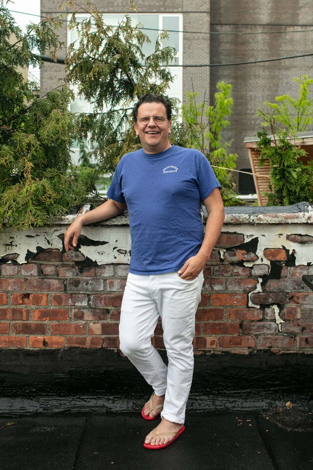 Ignacio Jimenez, wearing blue shirt, white jeans and flip flops, outside on roof, trees in background
