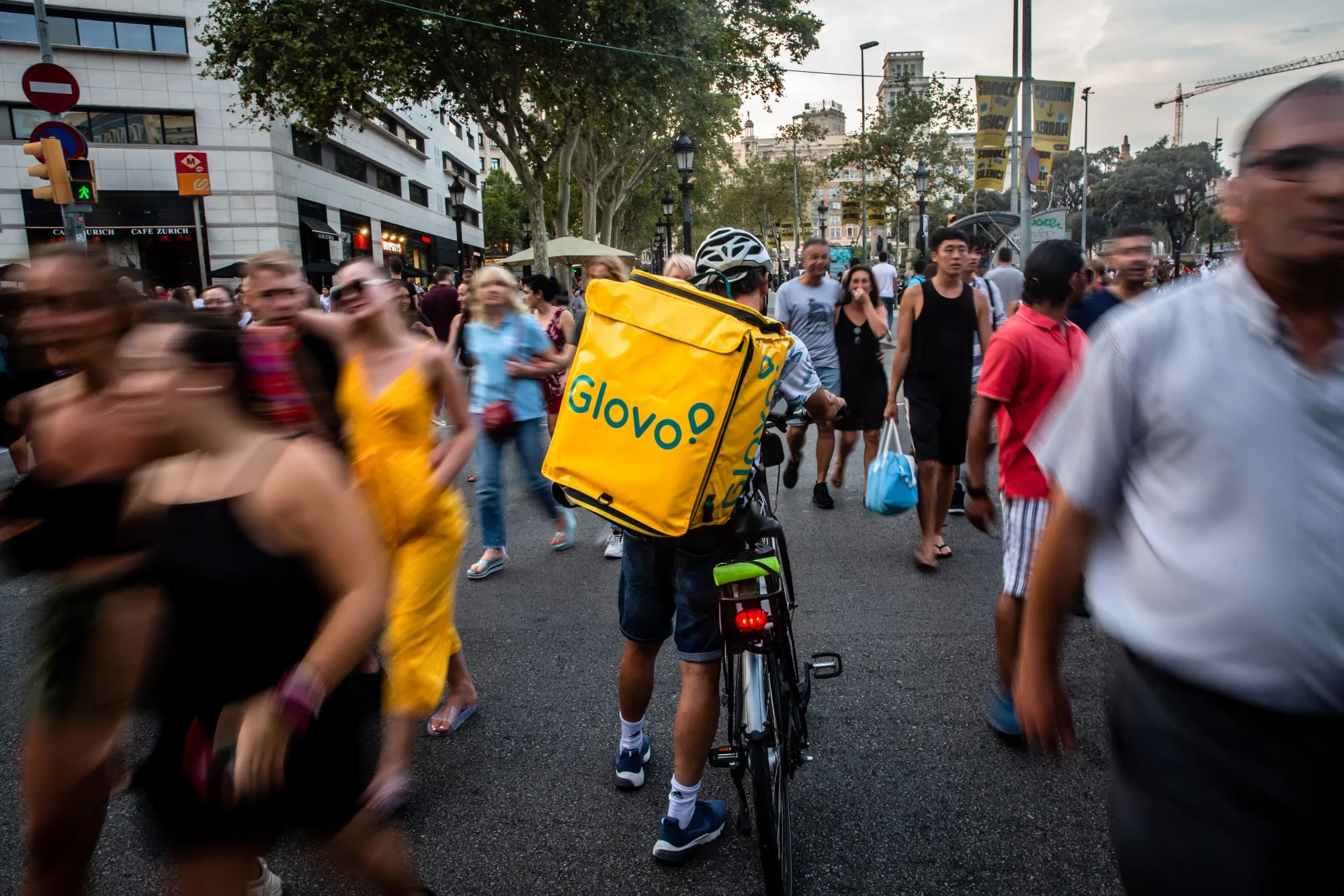A courier for Glovo wheels a bicycle through crowds in Barcelona, Spain.
