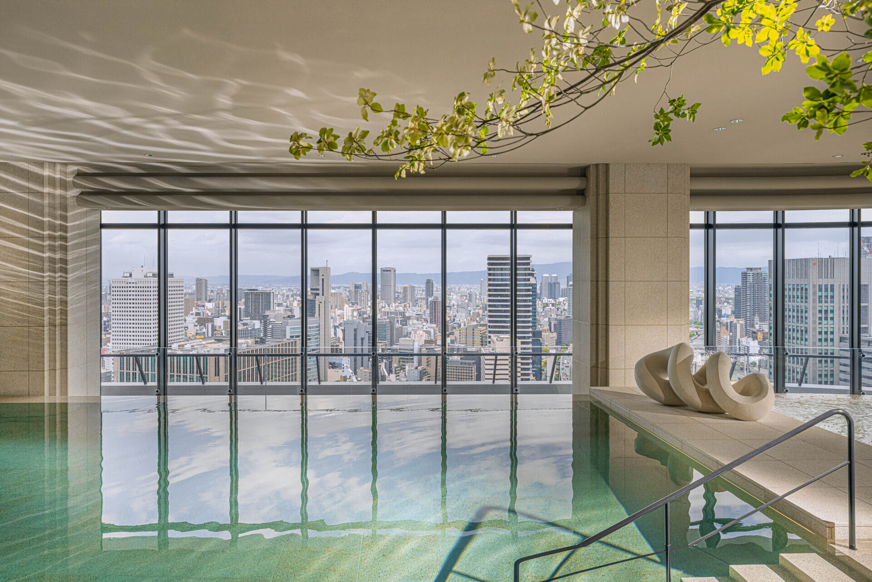 An indoor pool faces a wall of windows against the Osaka skyline.