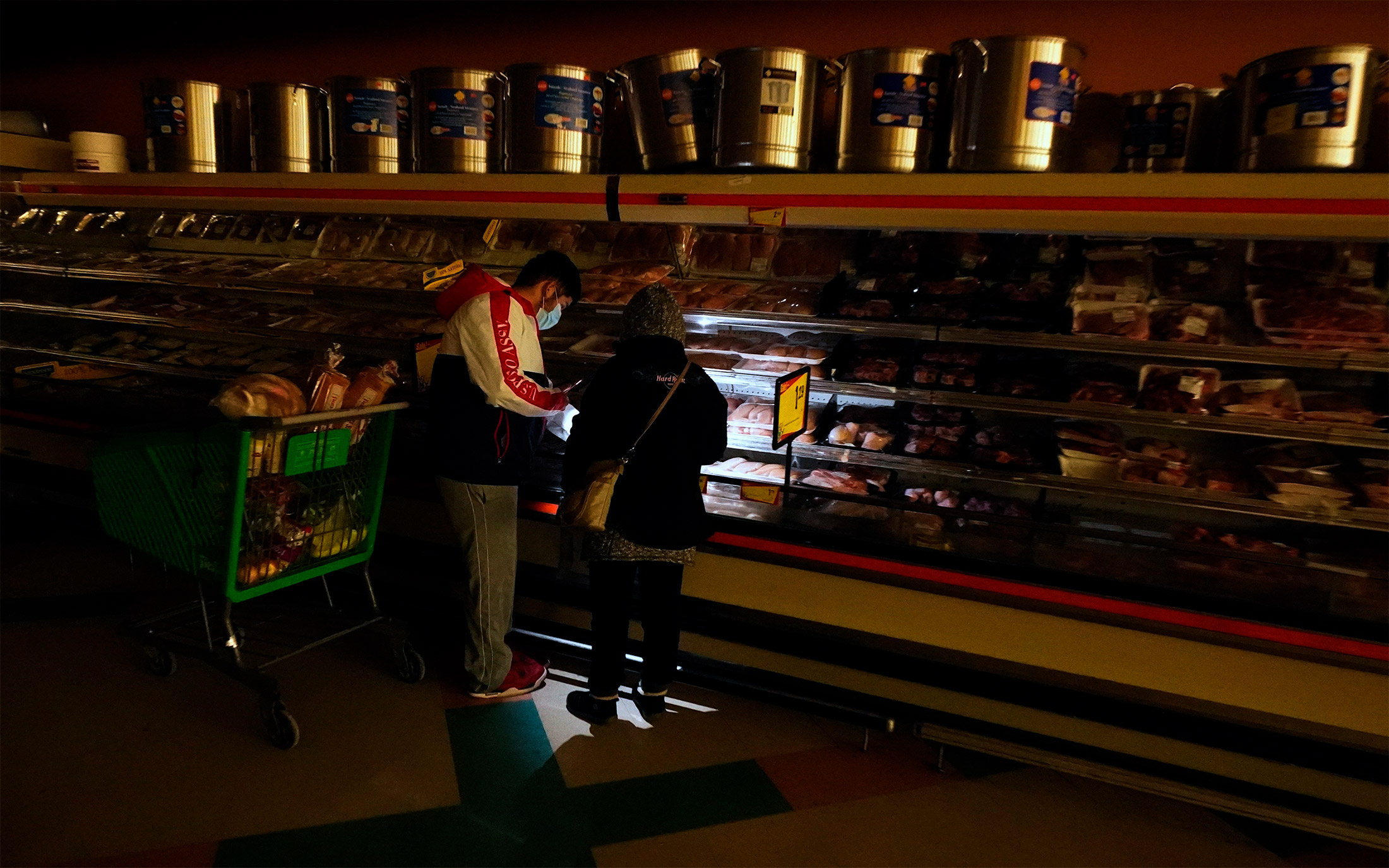 Customers use the light from a cell phone to look in the meat section of a grocery store in Dallas on Feb. 16.