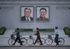 In a photo taken on June 4, 2017 men push their bicycles past the portraits of late North Korean leaders Kim Il-Sung (L) and Kim Jong-Il (R), on Kim Il-Sung square in Pyongyang.