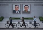 In a photo taken on June 4, 2017 men push their bicycles past the portraits of late North Korean leaders Kim Il-Sung (L) and Kim Jong-Il (R), on Kim Il-Sung square in Pyongyang.