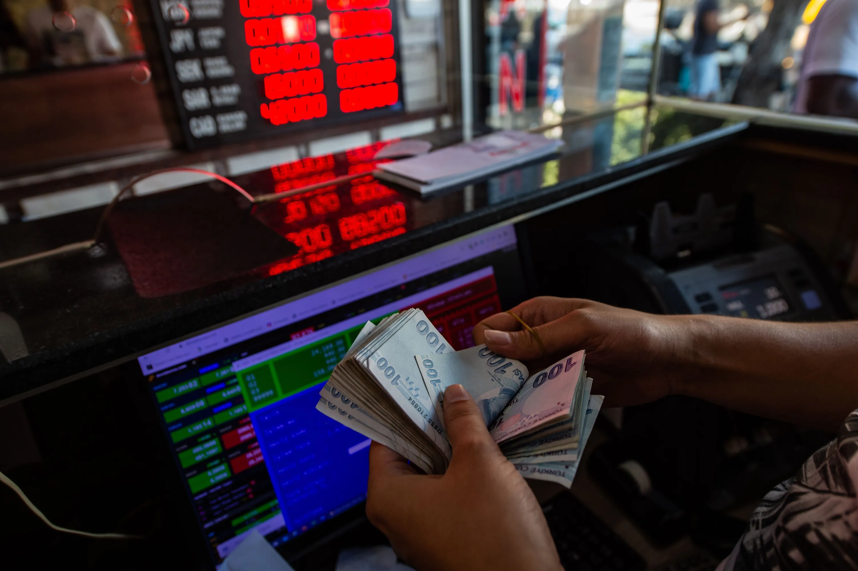 A currency exchange office worker counts Turkish Lira banknotes in front of the electronic panel displaying currency exchange rates at an exchange office in Istanbul, on Aug. 6.