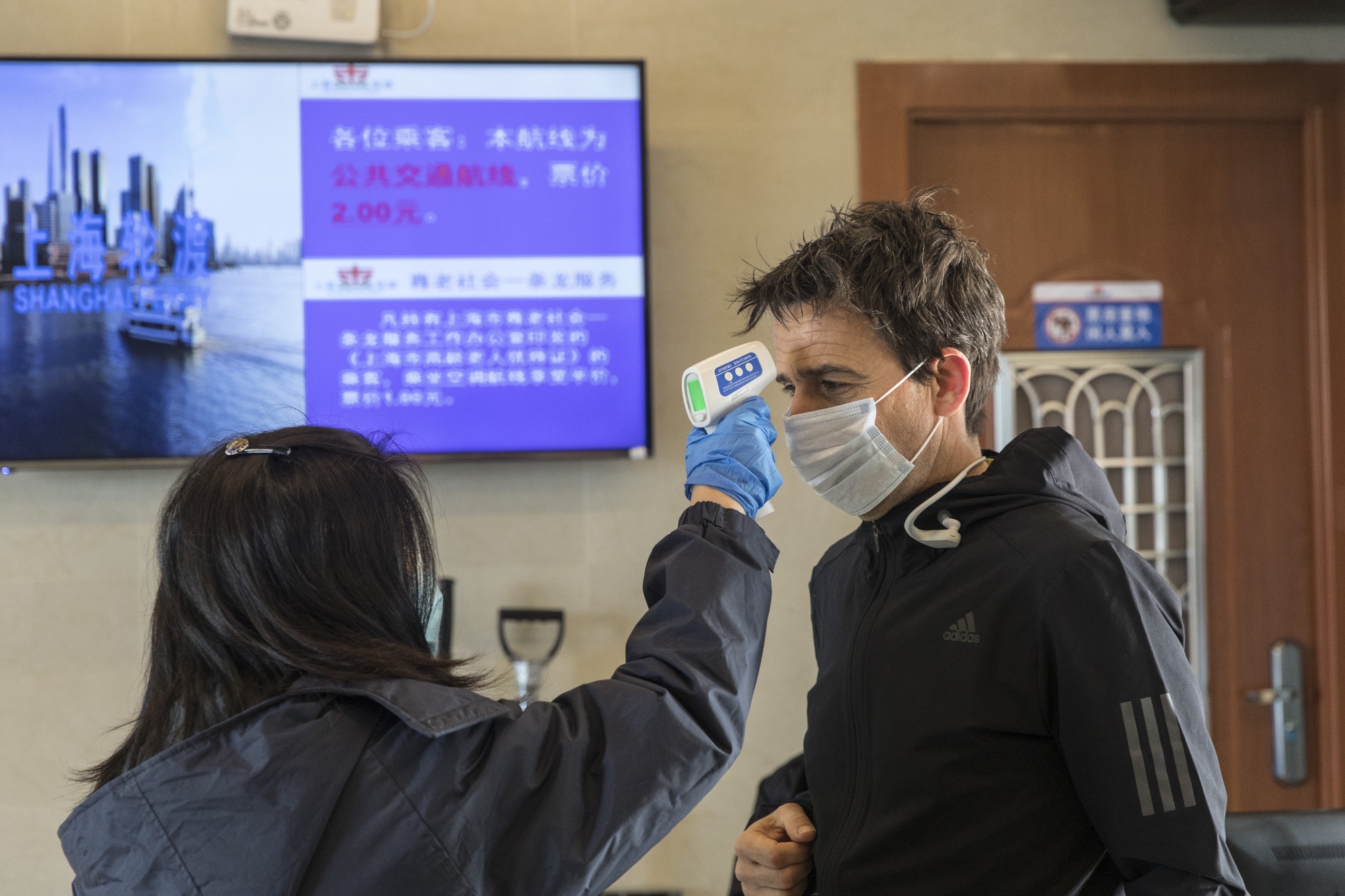 A transit worker takes the temperature of a passenger during a screening at a passenger ferry terminal in Shanghai on Jan. 30.