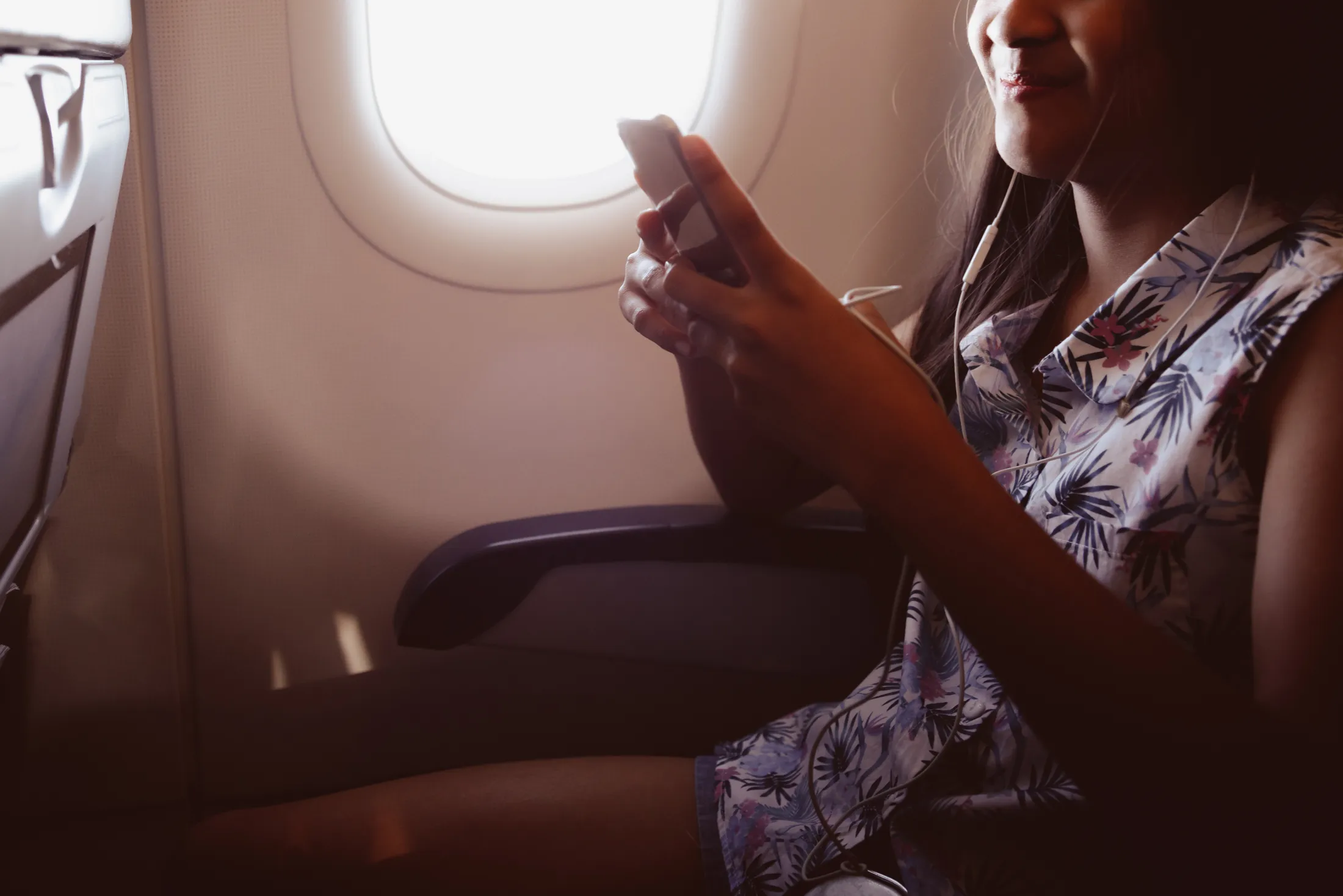 Adorable little girl traveling by an airplane child sitting by aircraft window and listen music