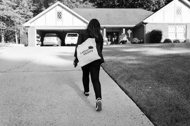 Murvartian walks towards a home carrying a tote bag that reads "Latino Victory" while canvassing. 