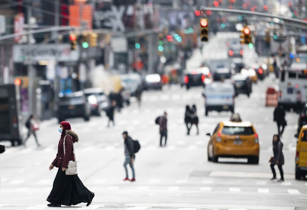A woman wearing a mask crosses the street in Times Square in New York City. 