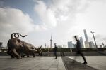 Pedestrians walk past the Bund Bull statue as skyscrapers of the Pudong Lujiazui Financial District stand across the Huangpu River in Shanghai.