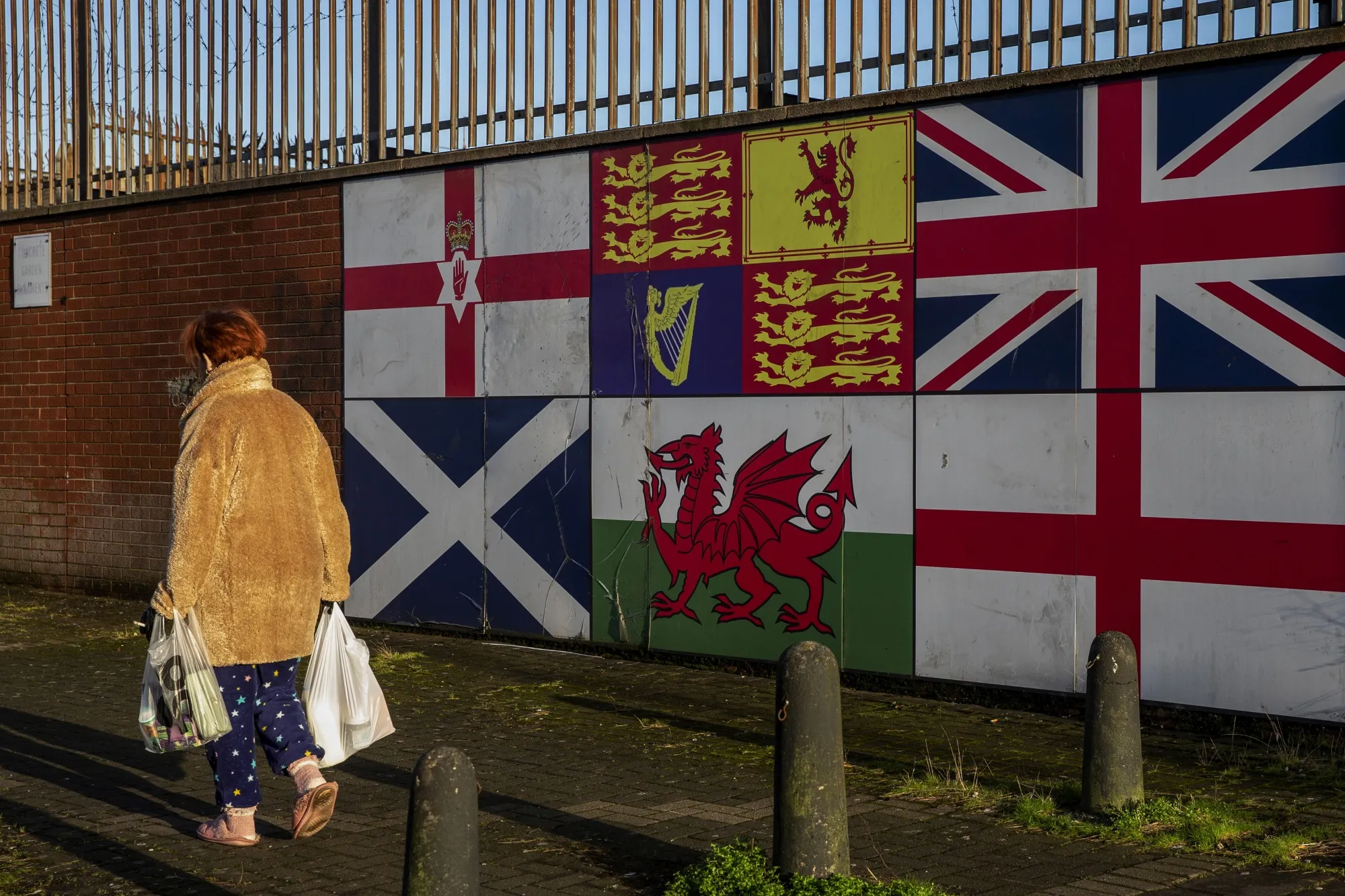 A pedestrian passes a display of national flags, clockwise from top left, of the Ulster Banner, the Royal Standard, British Union Flag, Scotland, Wales,&nbsp;and England, in Belfast, Northern Ireland.