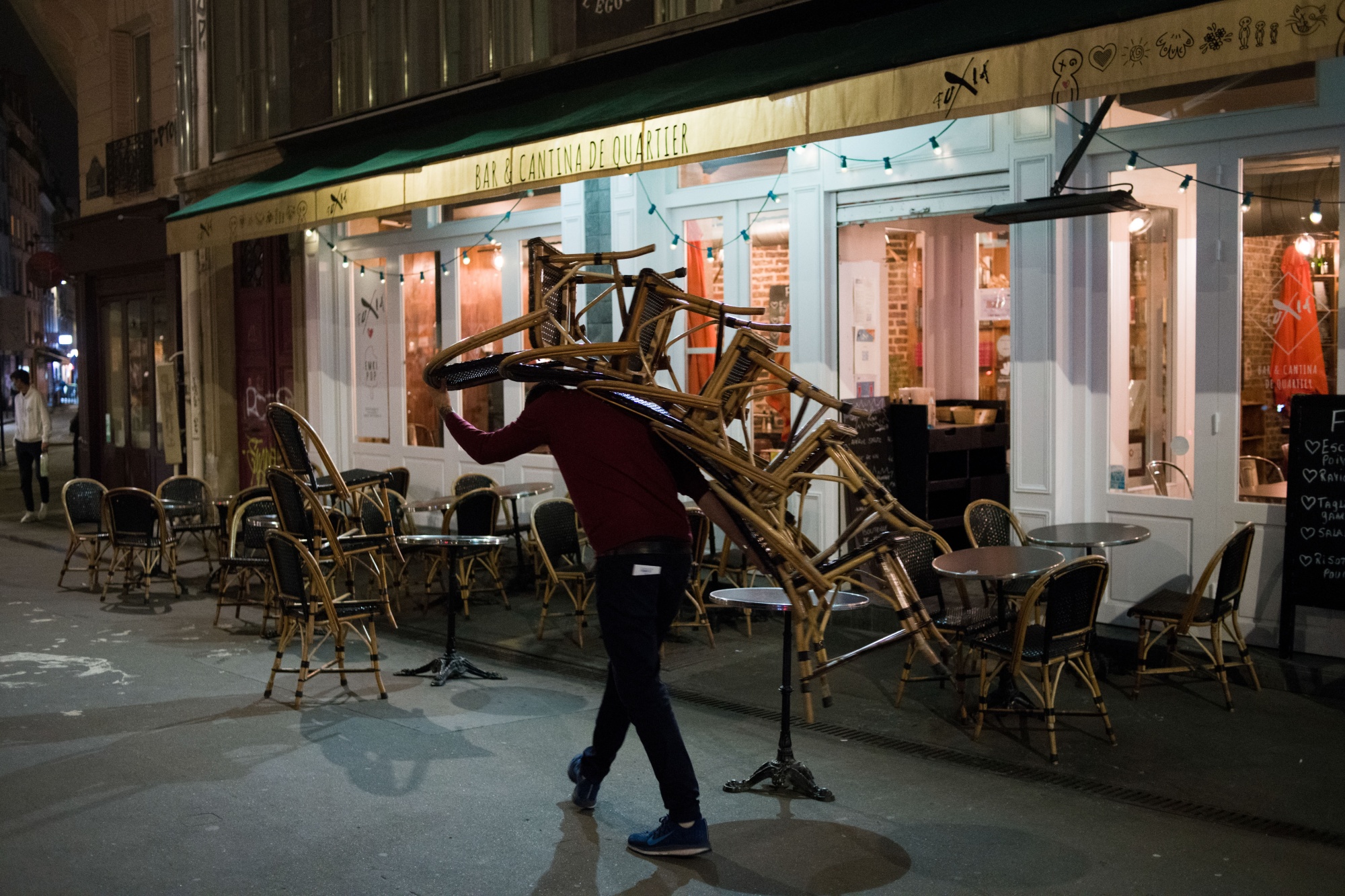 A waiter carries chairs from an outdoor dining section as a curfew comes into effect in Paris&nbsp;on&nbsp;Oct. 17.