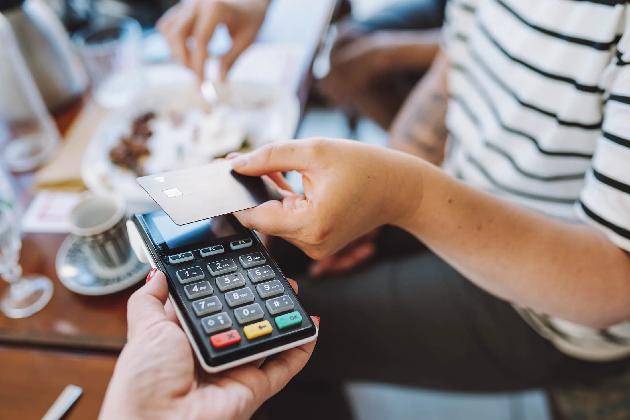 Tap to pay, cashless. Cropped woman hand holding credit card to pay in cafe for food and drinks. Focus on hand and card reader. Close up