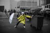 A protester wearing a hard hat, face mask and yellow poncho holds an open umbrella as a shield in front of him while standing in the middle of the street, throngs of protesters and press behind him.