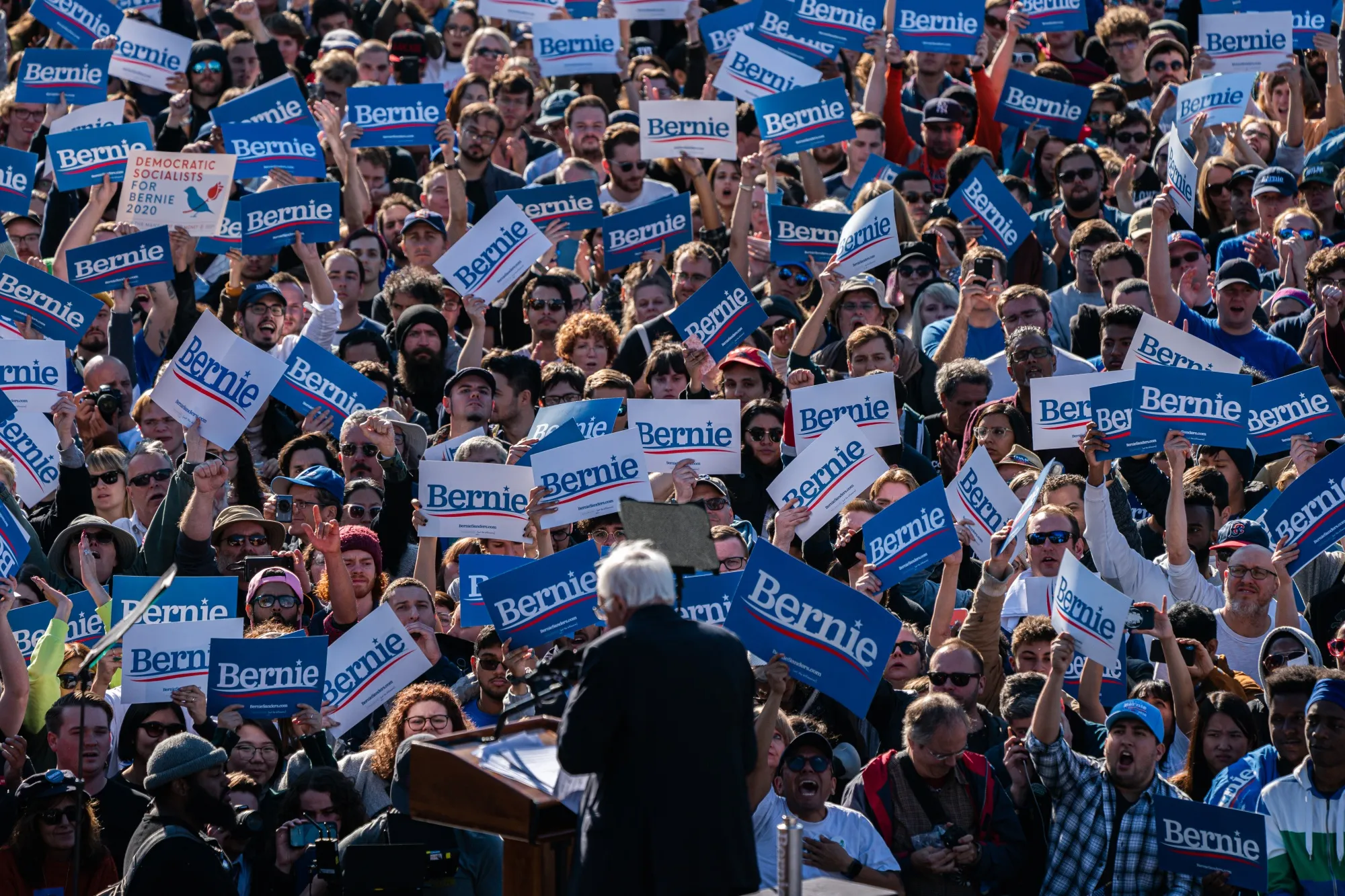 Attendees hold campaign signs during a rally with Senator Bernie Sanders.