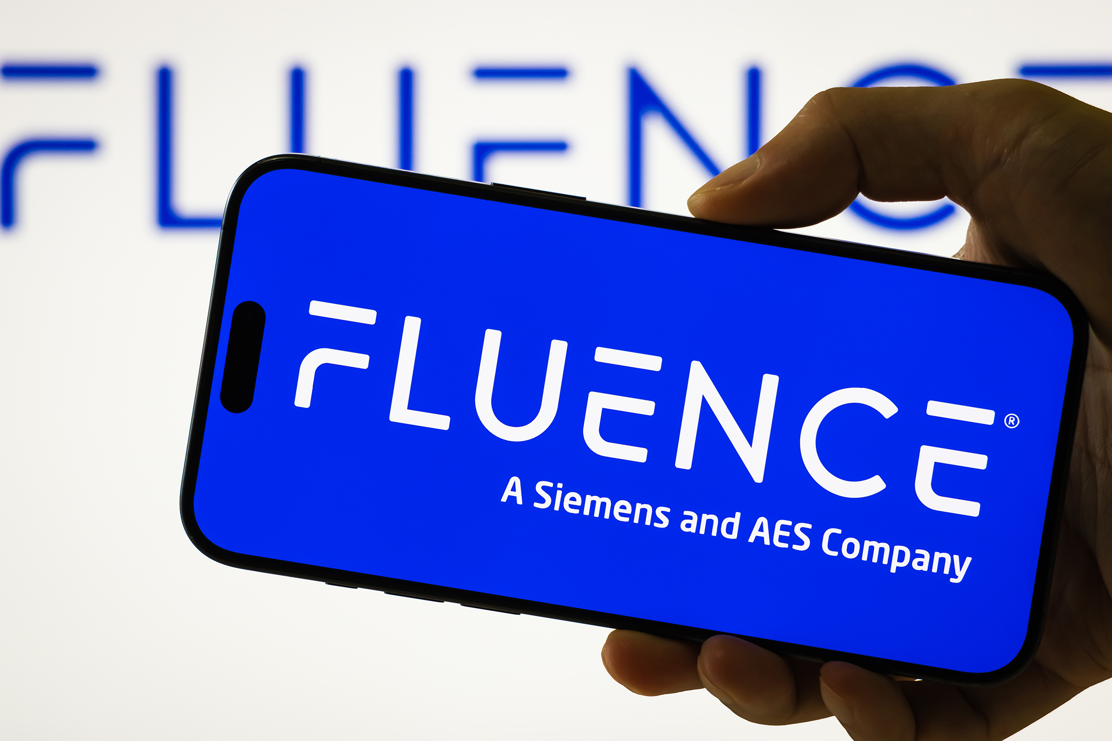 In this photo illustration, a person holds a smartphone displaying the logo of Fluence Energy Inc. (NASDAQ: FLNC), a global energy storage technology company formed as a joint venture between Siemens and AES, with the company's branding visible in the background, on August 8, 2025 in Chongqing, China.