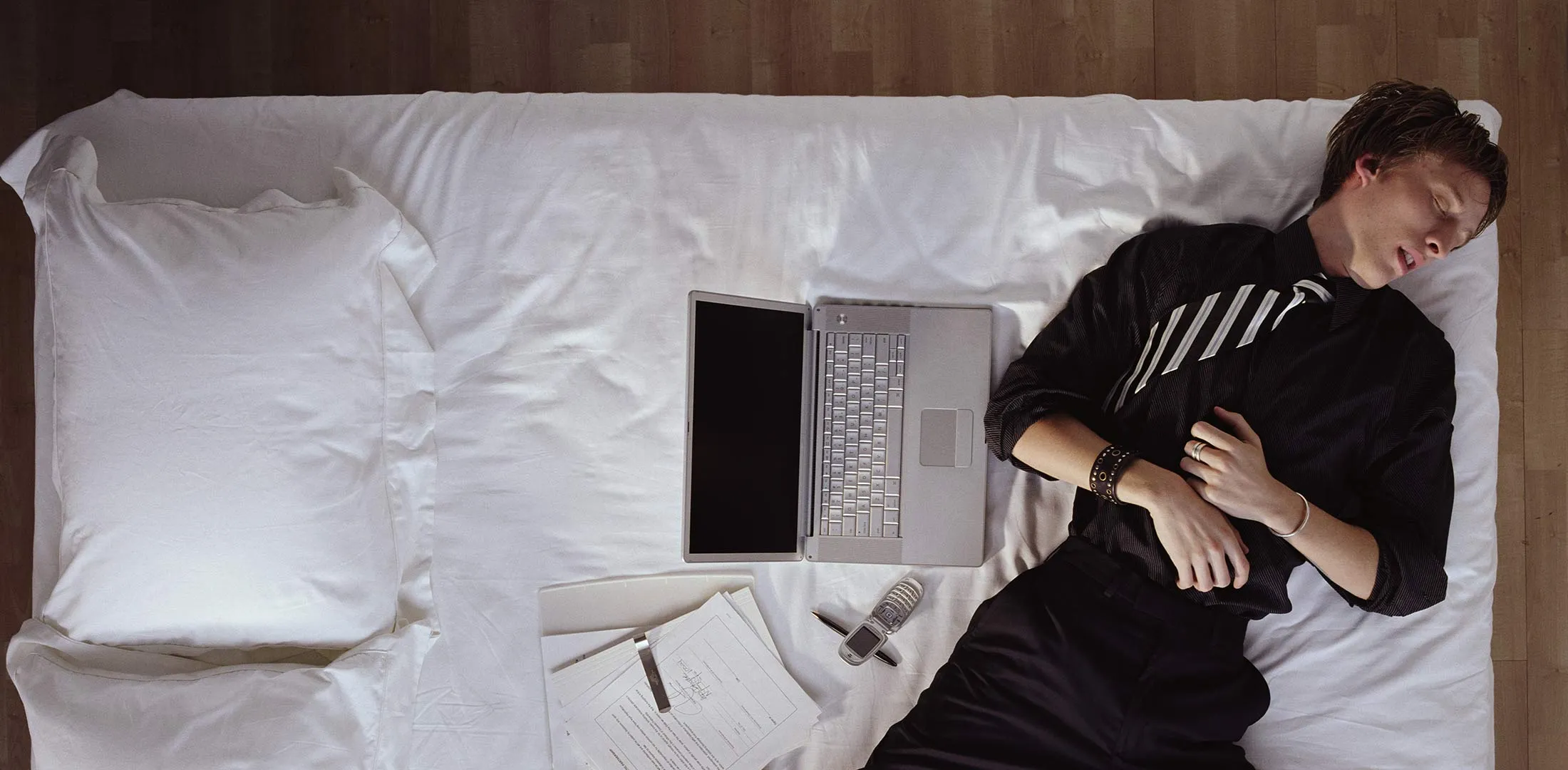 Young man in suit, sleeping on bed next to laptop, overhead view