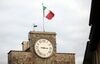 The Italian national flag flies atop a clock tower.