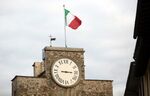 The Italian national flag flies atop a clock tower.