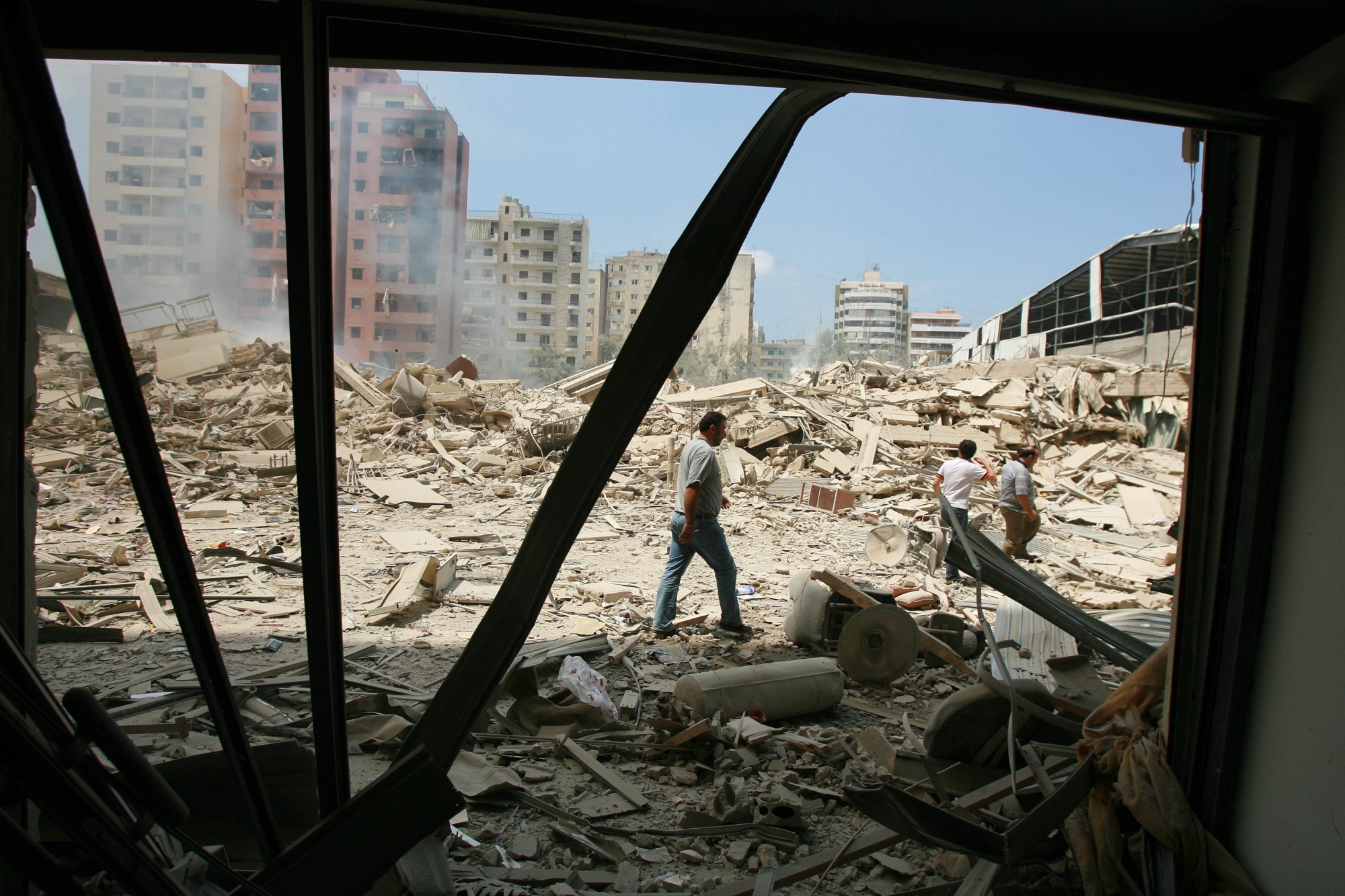 A man walks across a pile of rubble with buildings behind him.
