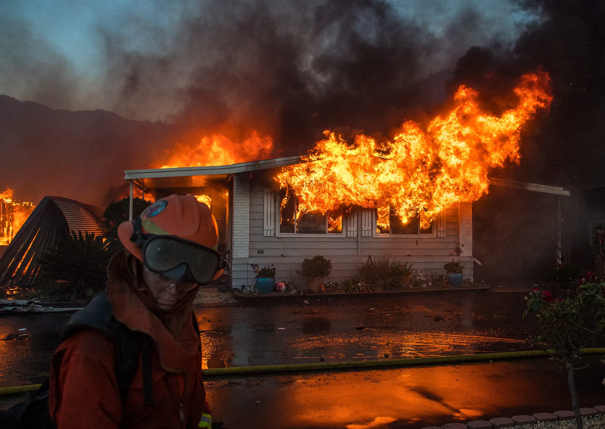 A firefighter turns away from the heat as flames explode through the front windows of a home burning in the Lilac fire&nbsp;in Pala Mesa, Calif.&nbsp;on Dec. 7, 2017.