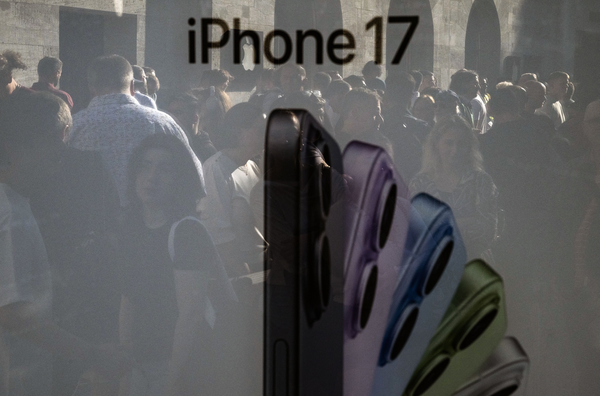Customers outside of an Apple store are reflected in an advertising panel in Berlin on Sept. 19, 2025, as the company's iPhone 17 was released.  Photographer: John MacDougall/AFP/Getty Images