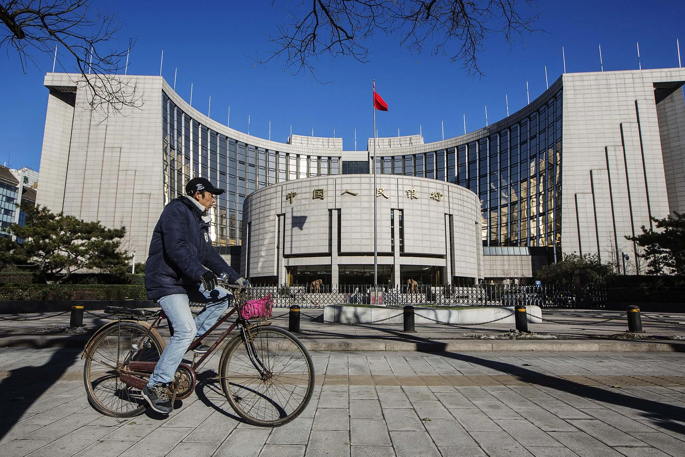 A man rides a bicycle past the People's Bank Of China (PBOC) headquarters in Beijing, China, on Wednesday, Dec. 2, 2015. China's great rebalancing -- the long-sought shift away from investment and manufacturing towards consumption and services -- is one of the nation's big themes of the year. One problem: the rebalancing stops at the water's edge.
