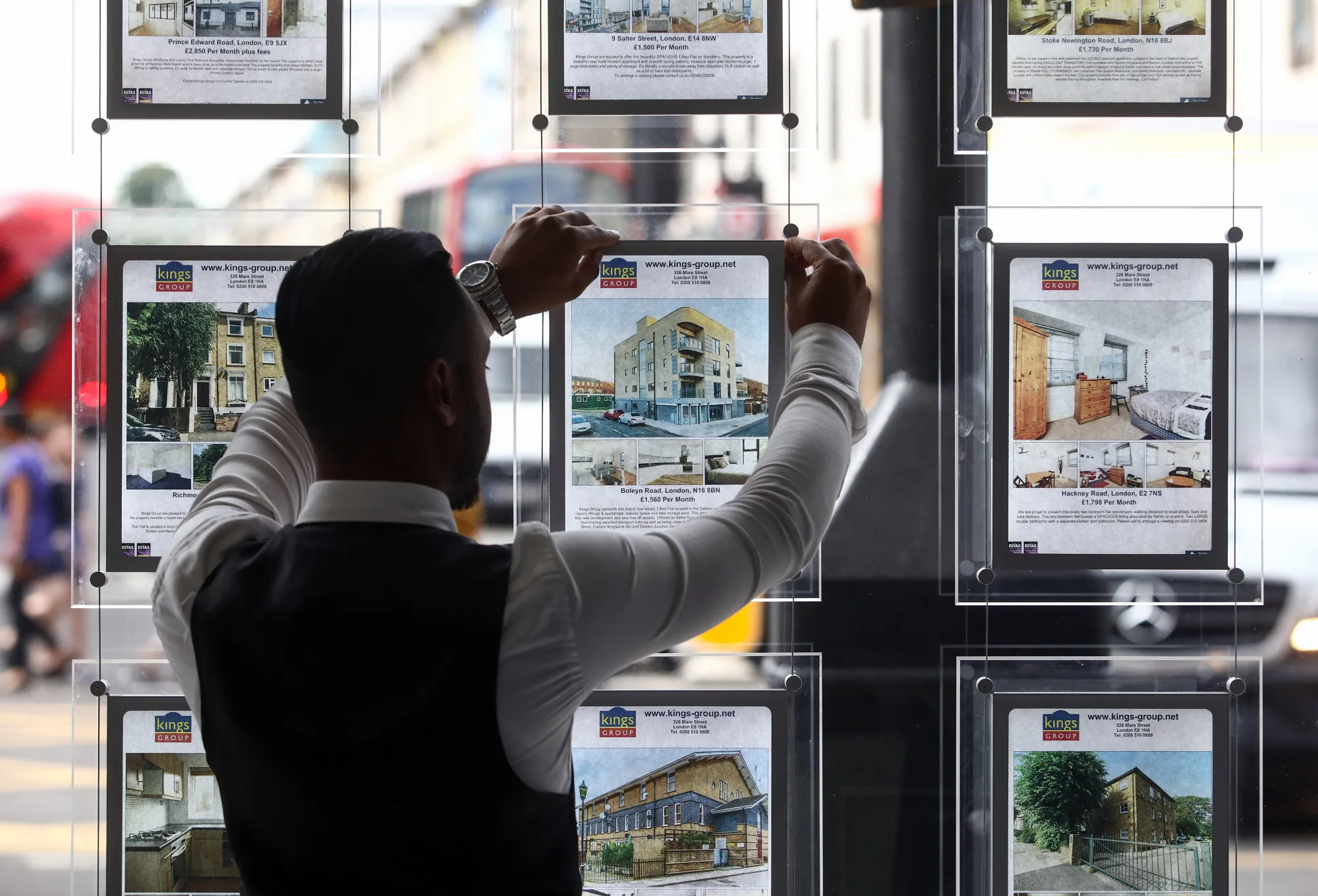 An employee places an advert for a residential house for sale into an estate agent's window in London.