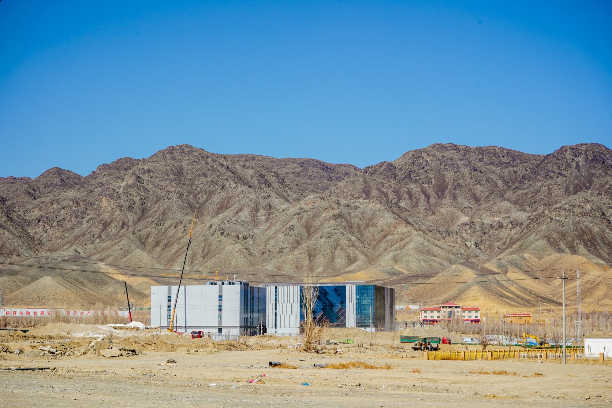 Photo showing a modern building in front of mountains. That is one of the data centers in Yiwu. Behind the building, there's a slogon painted on the wall, saying 'Data-electricity fusion shows great promise' in Chinese characters.