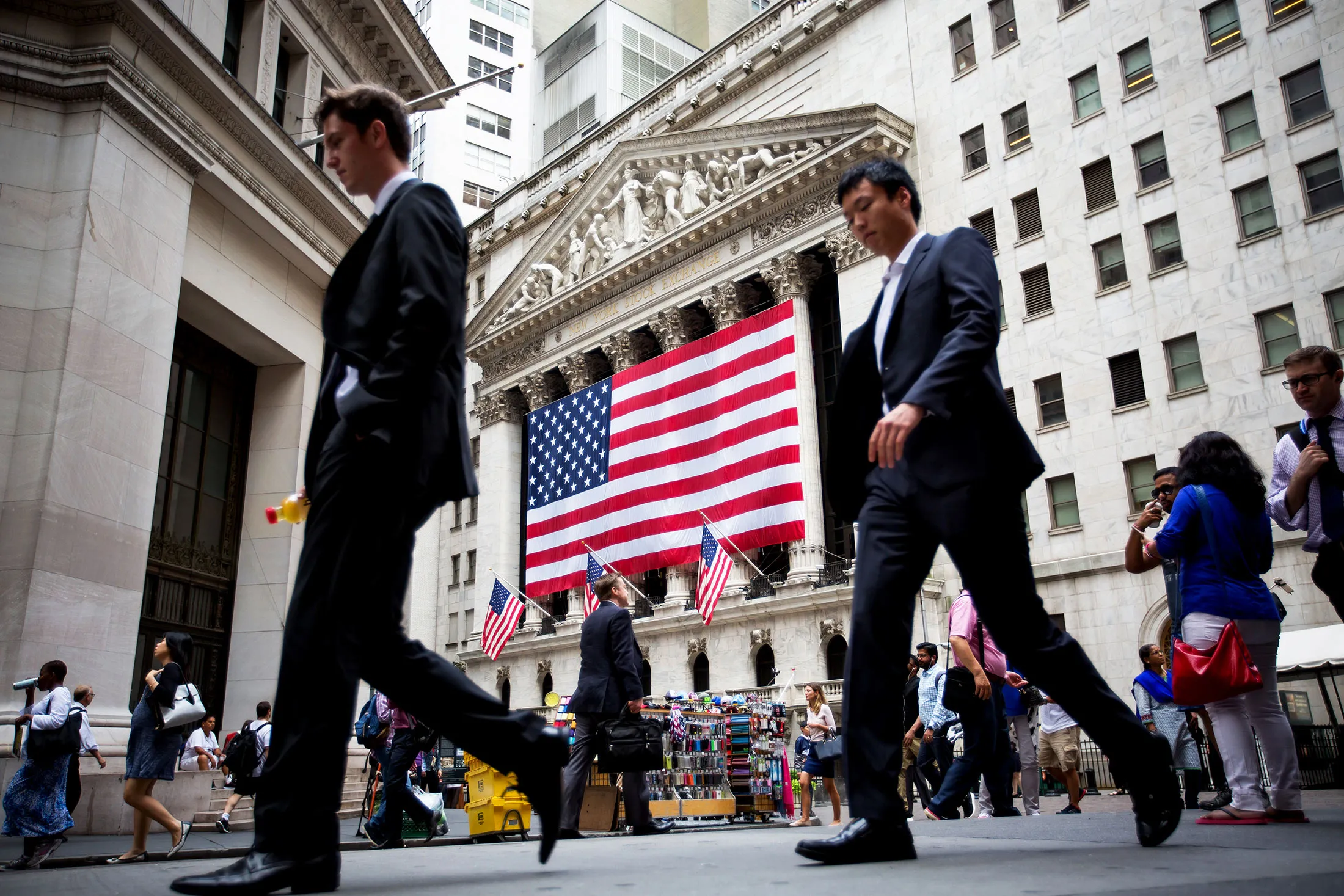 Pedestrians walk past the New York Stock Exchange (NYSE) in New York, U.S., on Tuesday, July 5, 2016. U.S. stocks slipped, tracking declines in European markets amid simmering concerns that Britain's exit from the European Union will further weigh on tepid global growth.
