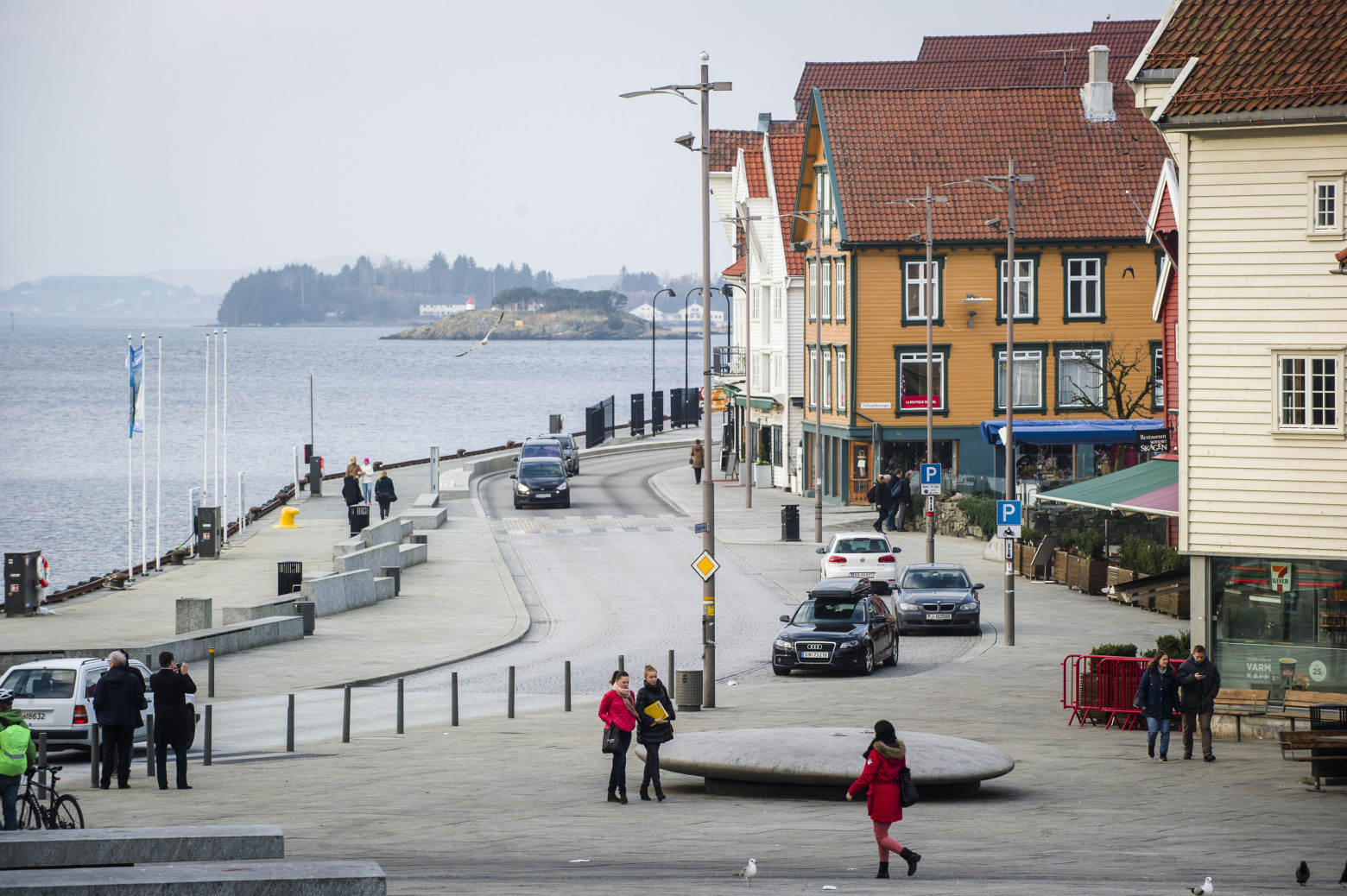 Pedestrians walk along the waterside past old buildings near the dock and port area in Stavanger.