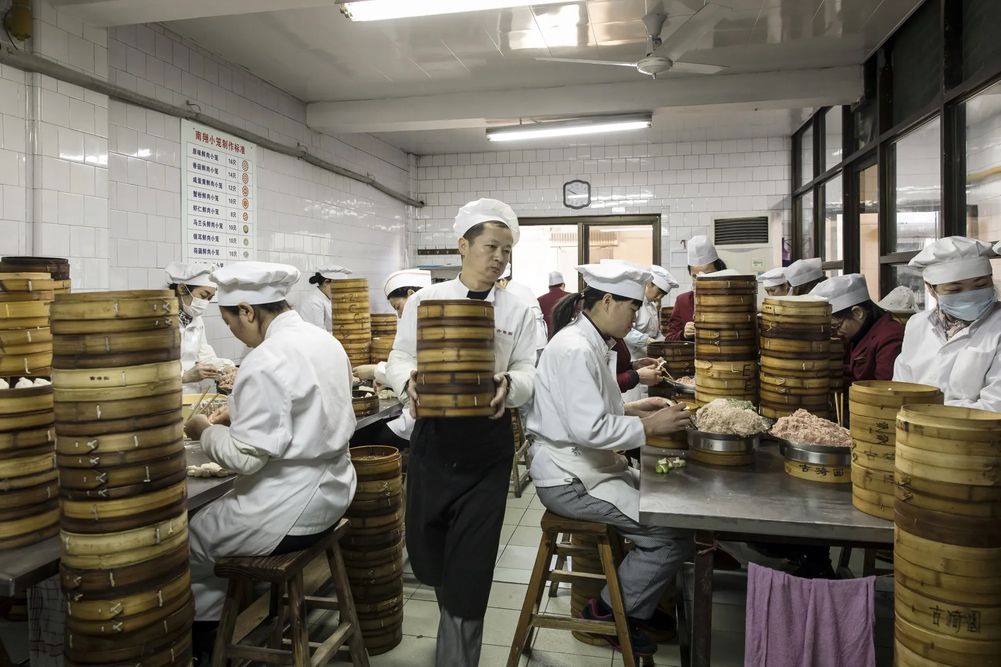 An employee carries a stack of bamboo steamer baskets as cooks make xiaolongbao dumplings in the kitchen at a restaurant in Shanghai.