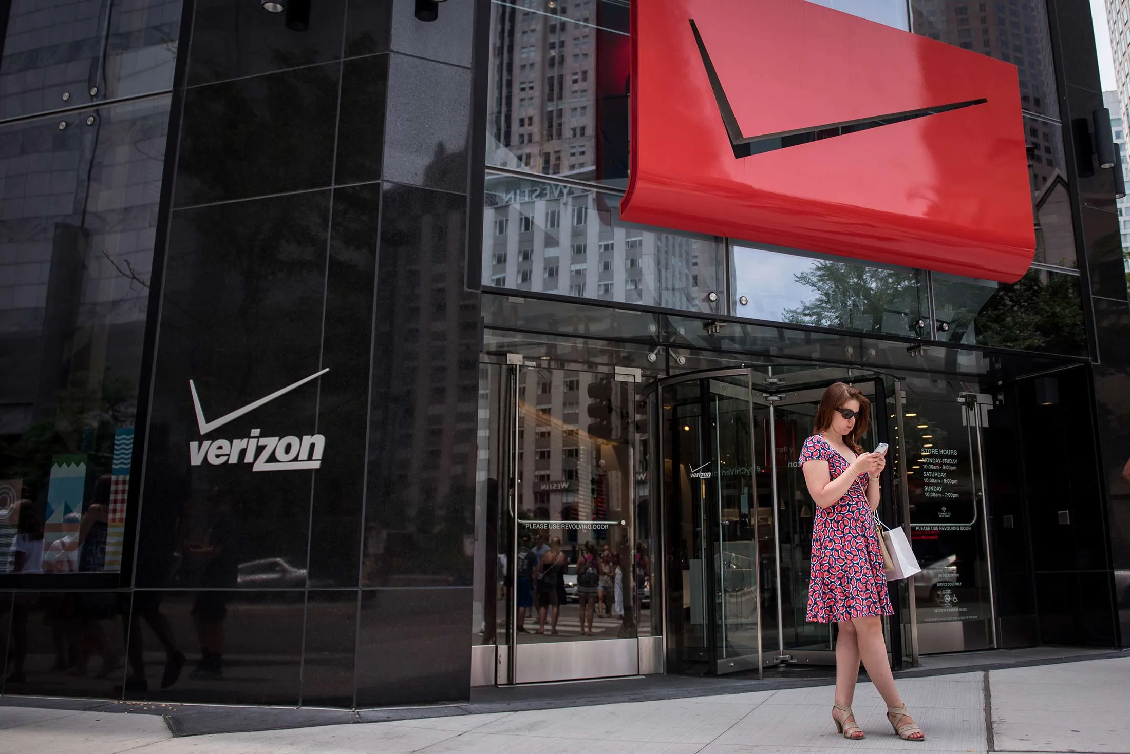 A pedestrian uses a smartphone outside a Verizon Communications Inc. store in downtown Chicago, Illinois, U.S., on Saturday, July 23, 2016. Verizon, who agreed to buy Yahoo! Inc.'s web assets for $4.83 billion, is scheduled to release earnings data on July 26.
