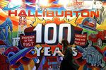 An attendee views a mobile device while walking in front of a mural displaying Halliburton Co. imagery during the 2019 Offshore Technology Conference (OTC) in Houston, Texas.