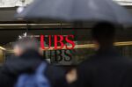 A pedestrian shelters under an umbrella while passing a UBS Group AG bank branch in Zurich, Switzerland.