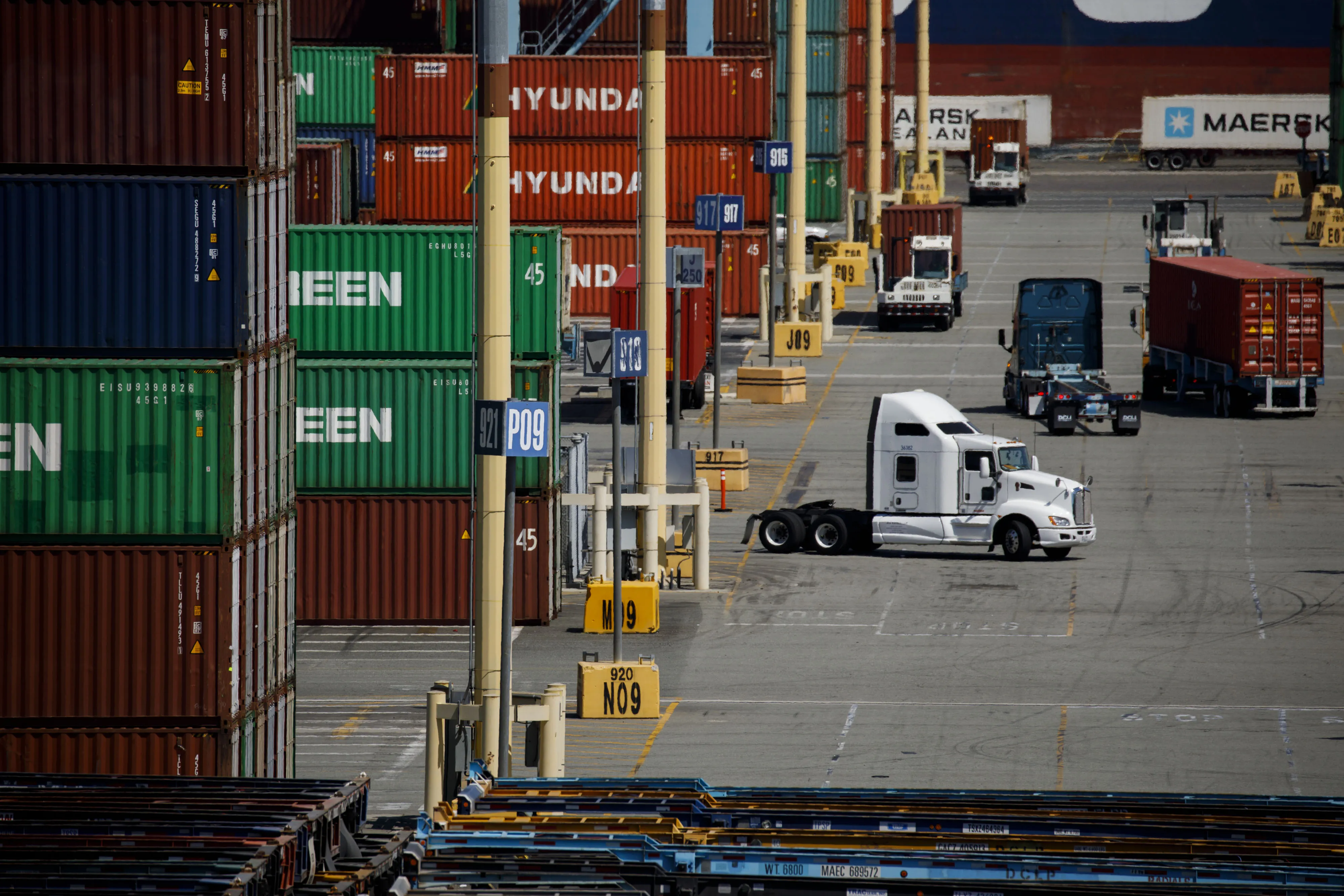 Semi-trucks drive past shipping containers in the APM shipping terminal at the Port of Los Angeles.&nbsp;