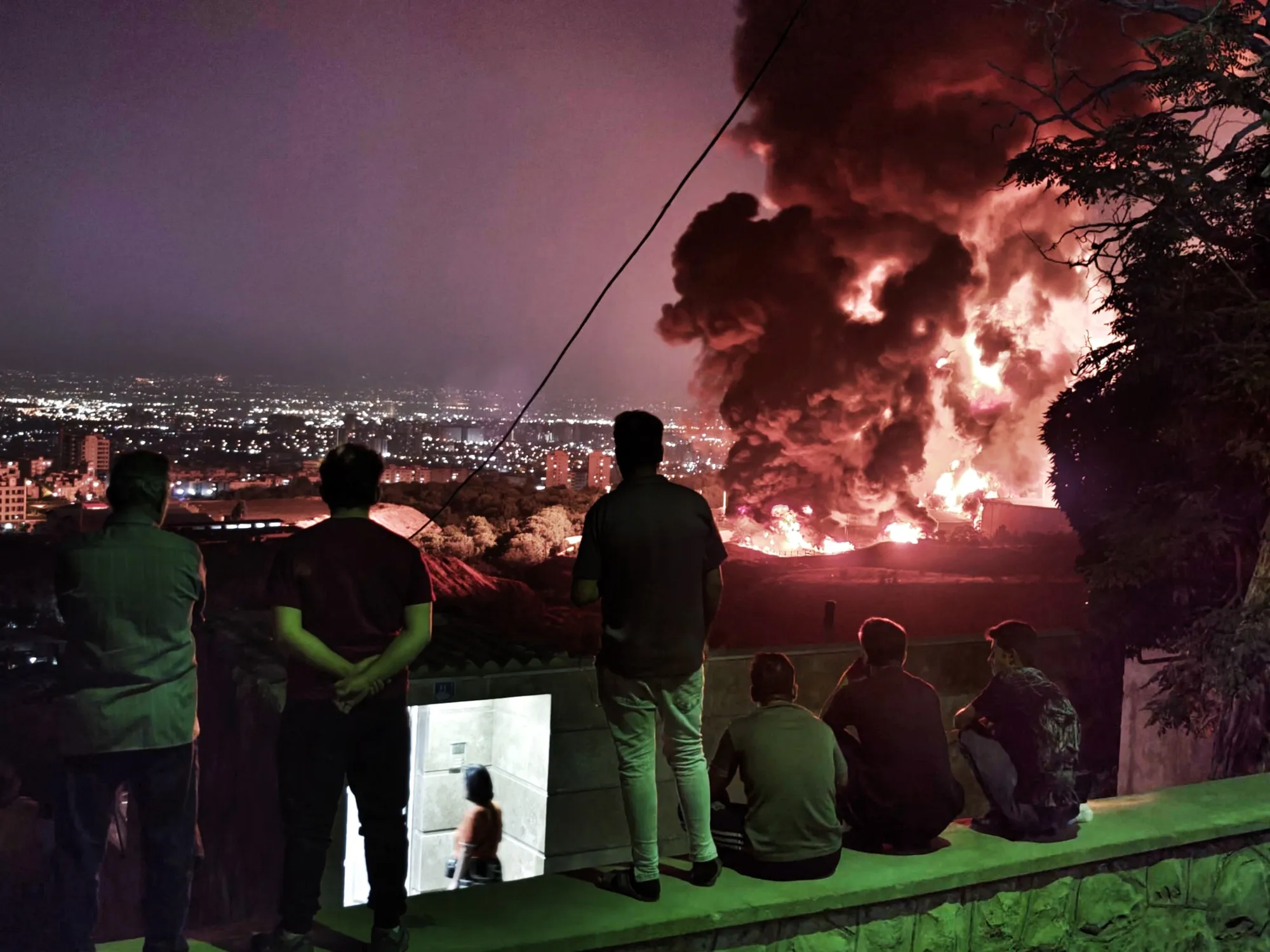 People observe fire and smoke from an Israeli attack on the Shahran oil depot on June 15, 2025 in Tehran,&nbsp;