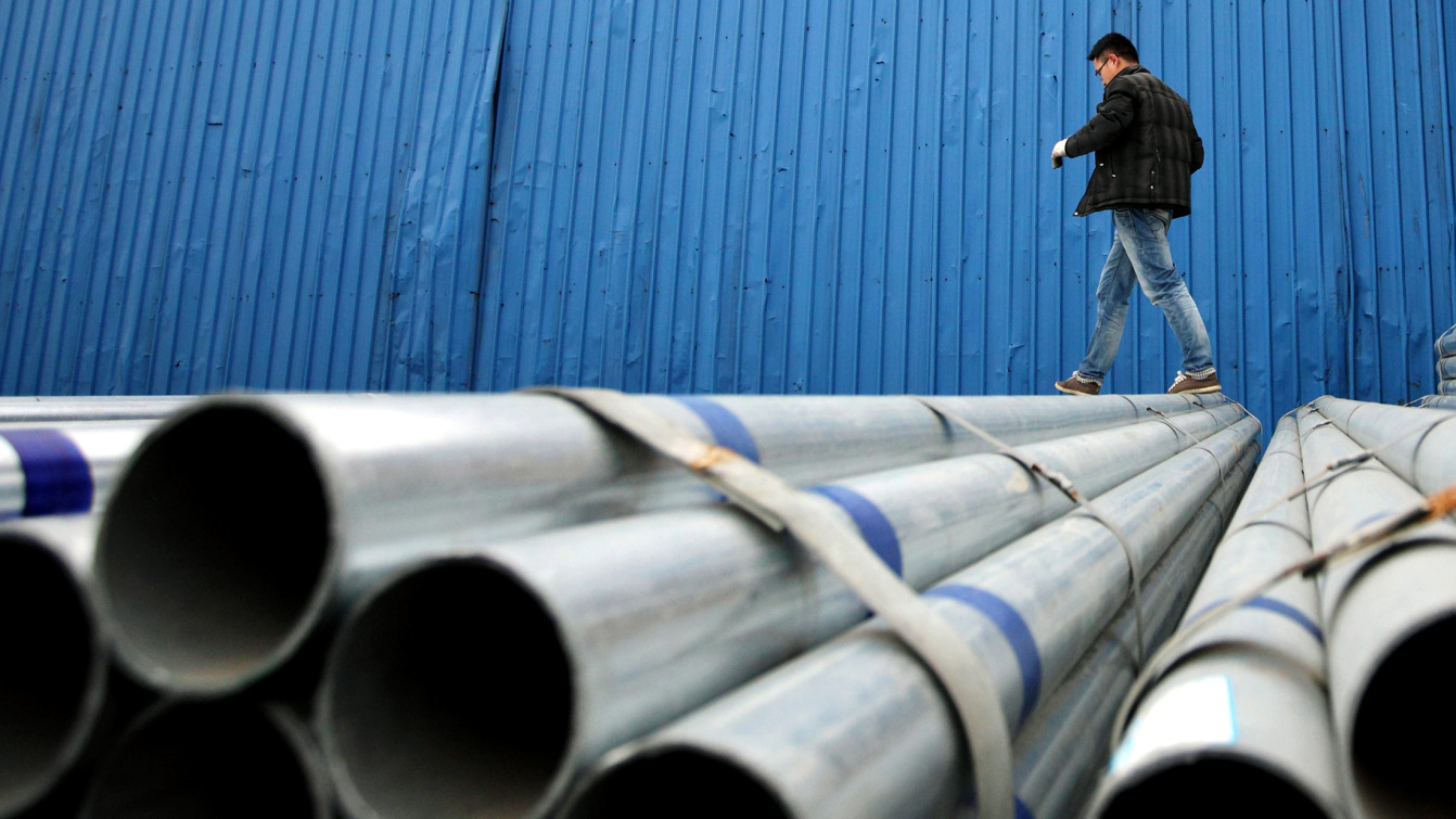 A worker walks on stacked steel pipes at a storage yard in Shanghai, China.
