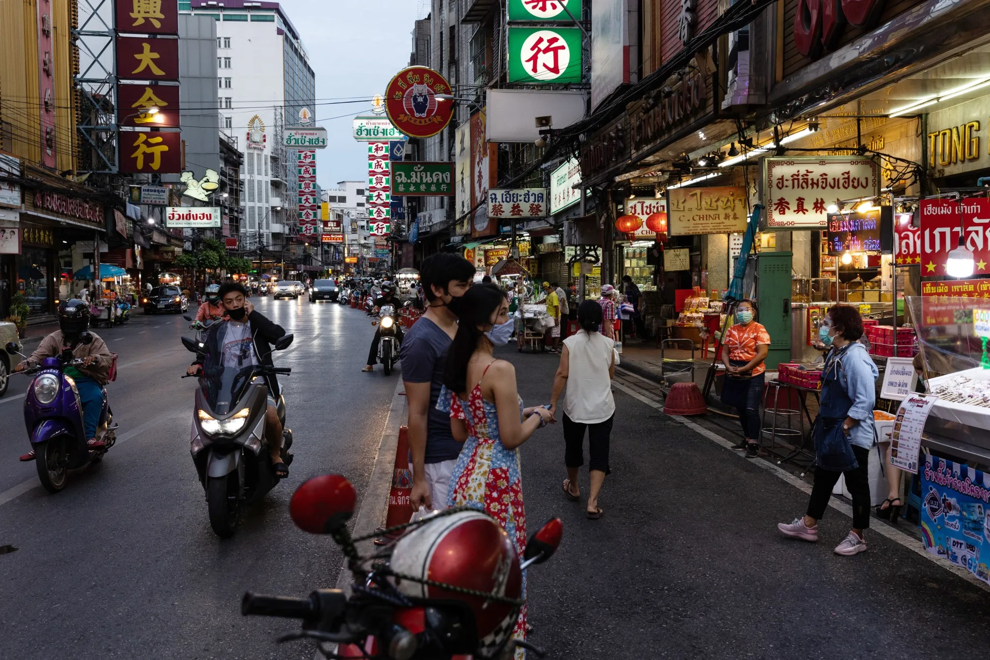 Motorcylists ride past pedestrians in Bangkok, Thailand.